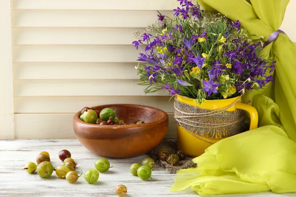 Mooi boeket van wilde bloemen in cup en bessen op houten tafel — Stockfoto