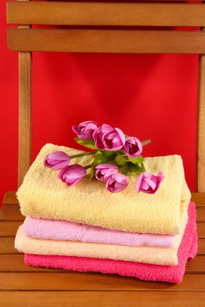 Ręczniki i kwiaty na drewniane krzesło na czerwonym tle — Zdjęcie stockowe