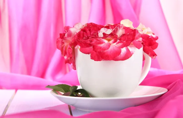 Roses en tasse sur table en bois sur fond de tissu rose — Photo