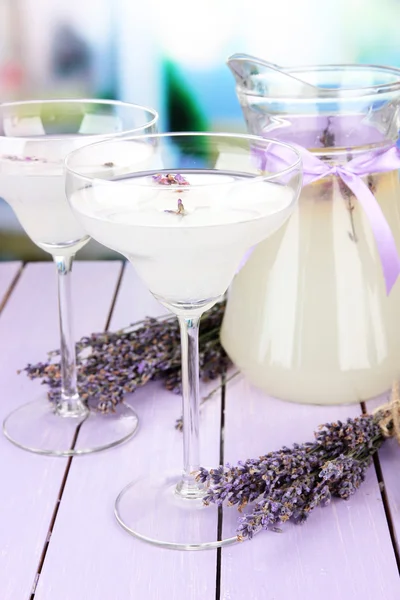 Lavender lemonade in glass jug and cocktail glasses, on bright background — Stock Photo, Image