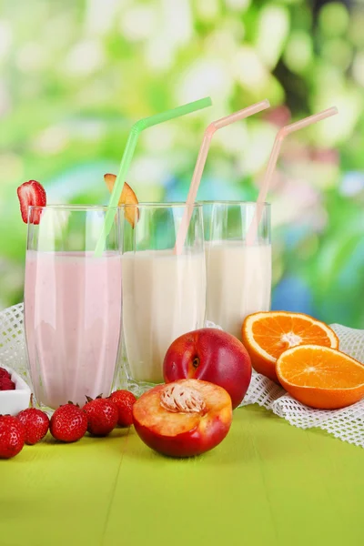 Delicious milk shakes with strawberries and peach on wooden table on natural background — Stock Photo, Image