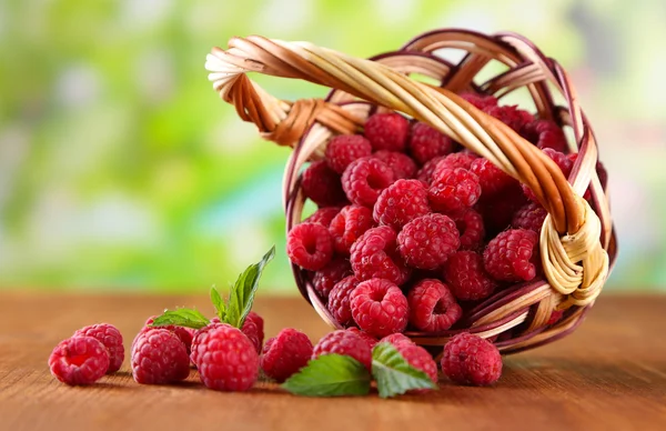 Ripe sweet raspberries in basket on wooden table, on green background — Stock Photo, Image