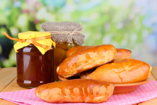 Fresh baked pasties with fruit jam, on wooden table, on bright background — Stock Photo, Image