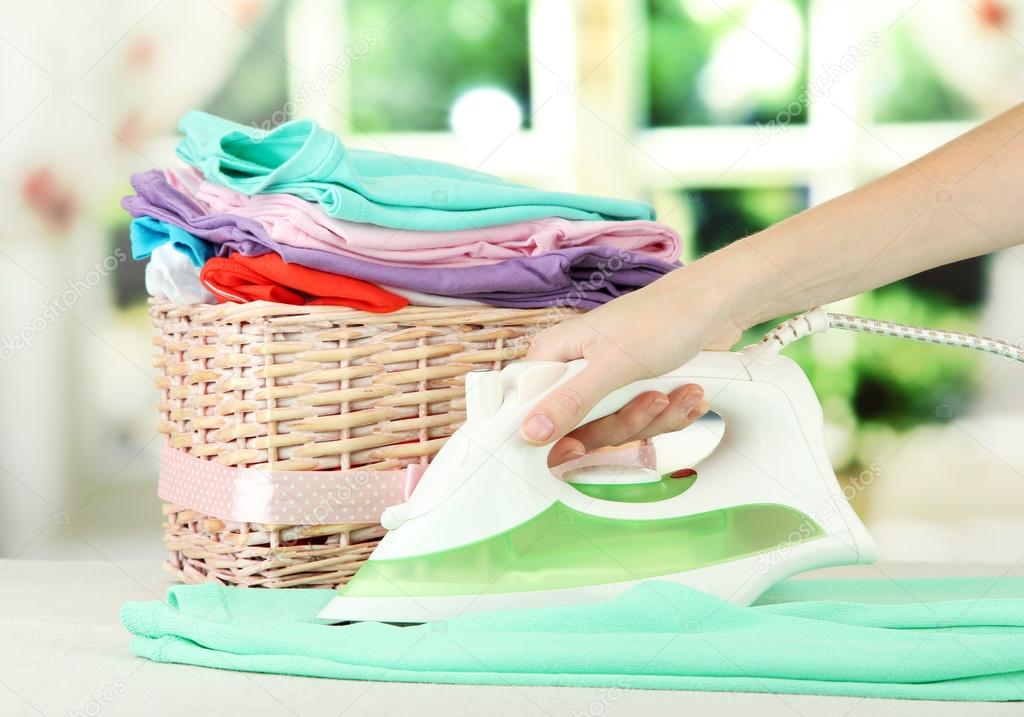 Woman's hand ironing clothes, on bright background