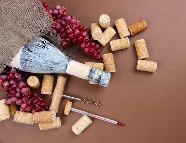 Vieja botella de vino, uvas y corchos sobre fondo marrón —  Fotos de Stock