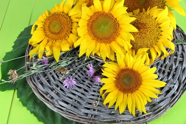 Beautiful sunflowers on wicker mat, on color wooden background — Stock Photo, Image
