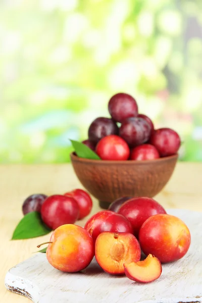 Ripe plums in bowl on wooden table on natural background — Stock Photo, Image