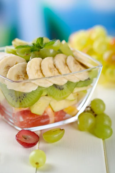 Salada de frutas saborosas em tigela de vidro, na mesa de madeira branca — Fotografia de Stock