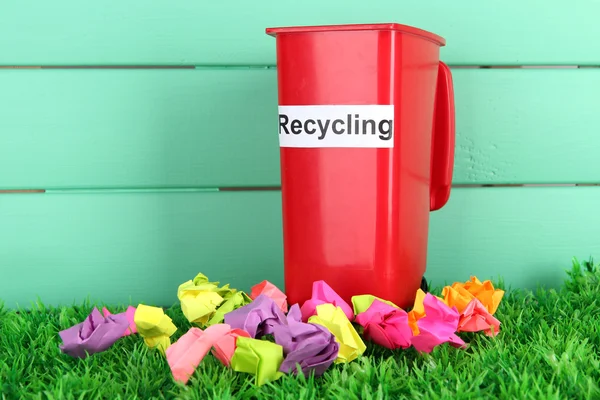 Recycling bin with papers on grass on light blue background — Stock Photo, Image