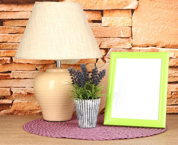 Marco de fotos colorido, lámpara y flores en la mesa de madera sobre fondo de pared de piedra — Foto de Stock