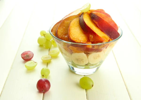 Smakelijke fruitsalade in glazen kom, op witte houten tafel — Stockfoto