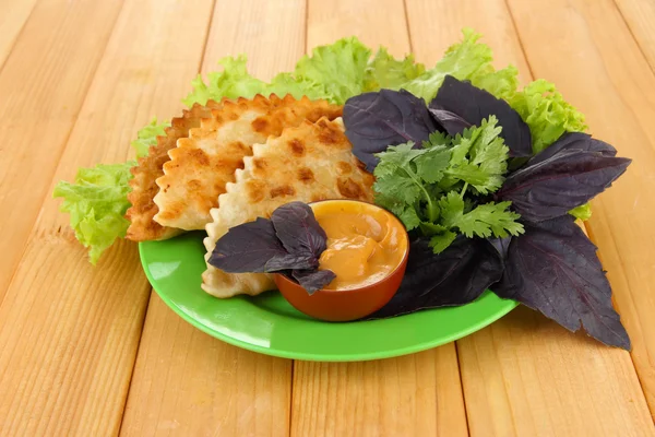 Tasty chebureks with fresh herbs on plate,on wooden background — Stock Photo, Image