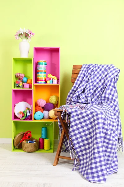 Colorful shelves of different colors with utensils near chair with plaid on wall background — Stock Photo, Image