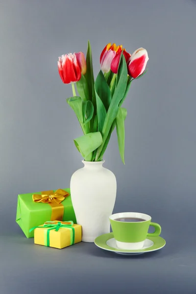 Beautiful tulips in bucket with gifts and cup of tea on grey background — Stock Photo, Image