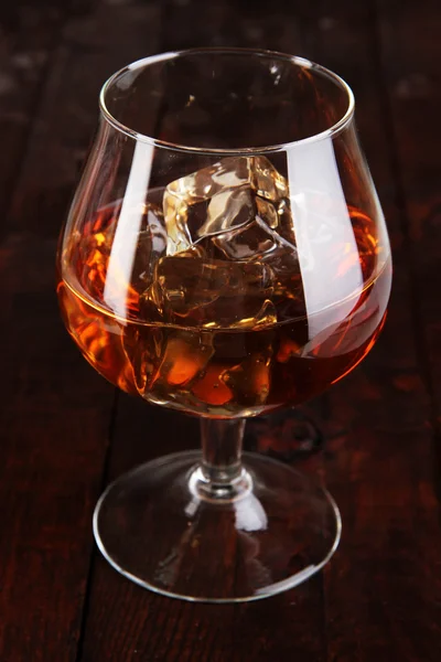 Brandy glass with ice on wooden background — Stock Photo, Image