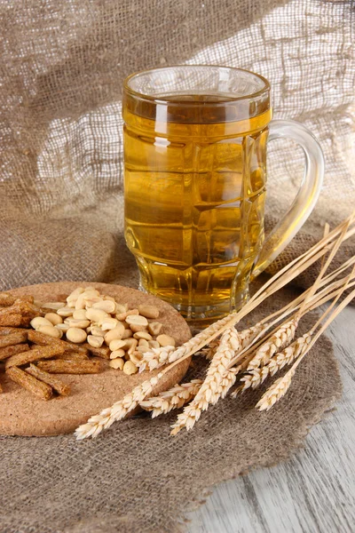 Beer in glass, crackers and nuts on bagging on wooden table