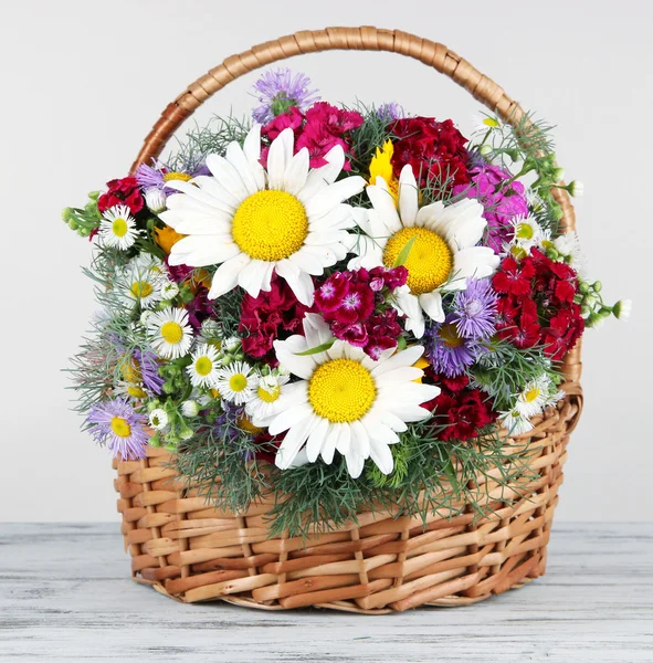Beautiful bright flowers in wicker basket on table on gray background — Stock Photo, Image
