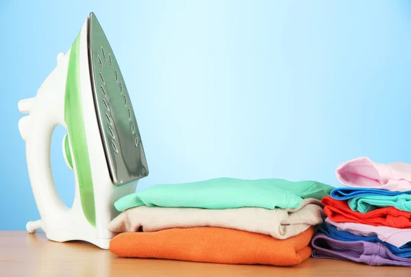 Steam iron with clothes, on color background — Stock Photo, Image