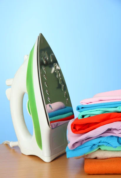 Steam iron with clothes, on color background — Stock Photo, Image