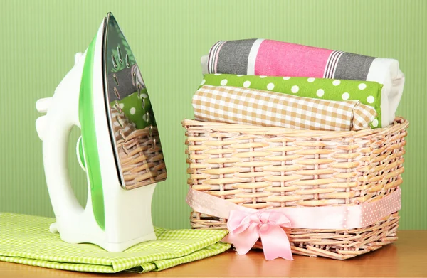 Steam iron and wicker basket with clothes, on color background — Stock Photo, Image