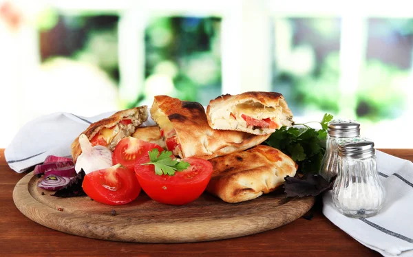 Pizza Calzones auf Holzbrett neben Serviette auf Holztisch auf Fensterhintergrund — Stockfoto