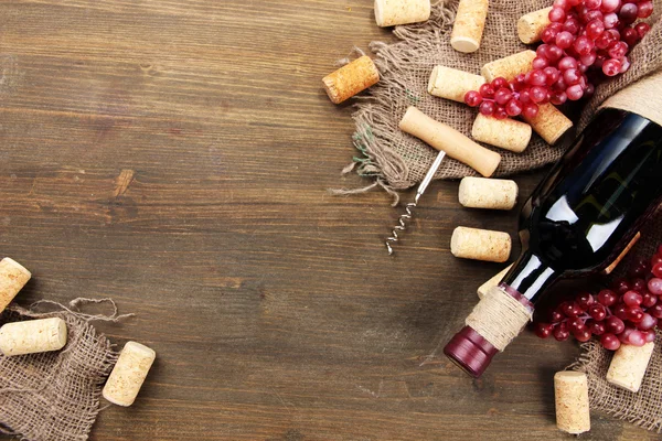 Botella de vino, uvas y corchos sobre fondo de madera — Foto de Stock