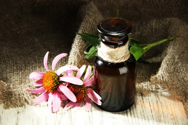 Medicine bottle with purple echinacea flowers on wooden table with burlap — Stock Photo, Image