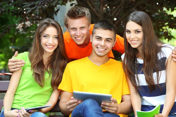 Happy group of young students sitting in park — Stock Photo, Image