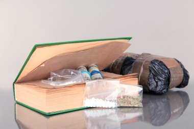 Narcotics in book-hiding place and packages on gray background clipart