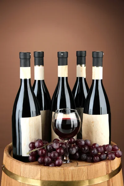 Composition of wine bottles, glasses and grape,on wooden barrel, on brown background — Stock Photo, Image