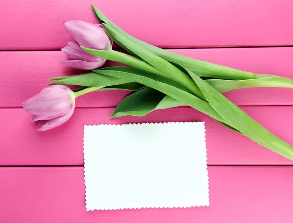 Schöner Strauß lila Tulpen und leere Karte auf rosa Holzhintergrund — Stockfoto