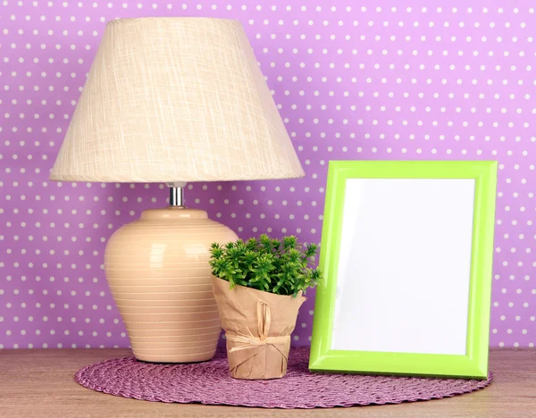 Marco de fotos colorido, lámpara y flores en la mesa de madera sobre fondo de lunares lila —  Fotos de Stock