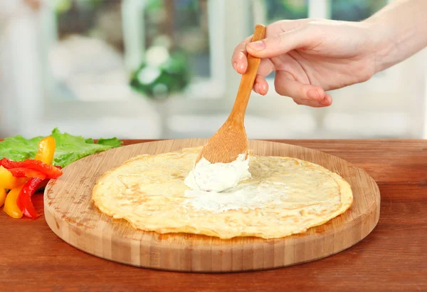 El proceso de la preparación de los rollos de huevo, sobre el fondo brillante: la mano femenina unta la crema de queso en la tortilla — Foto de Stock
