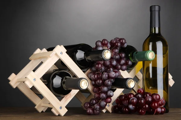Lahví vína na dřevěný stojan na šedém pozadí — Stock fotografie