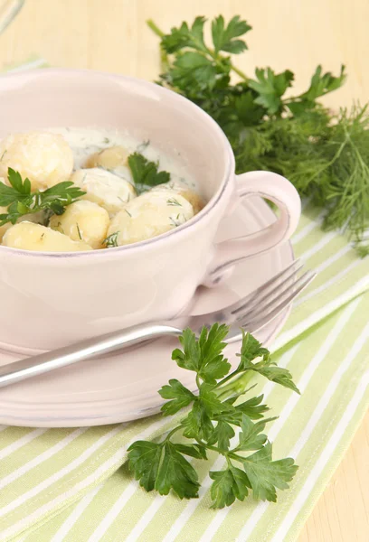 Tender young potatoes with sour cream and herbs in pan on wooden table close-up — Stock Photo, Image