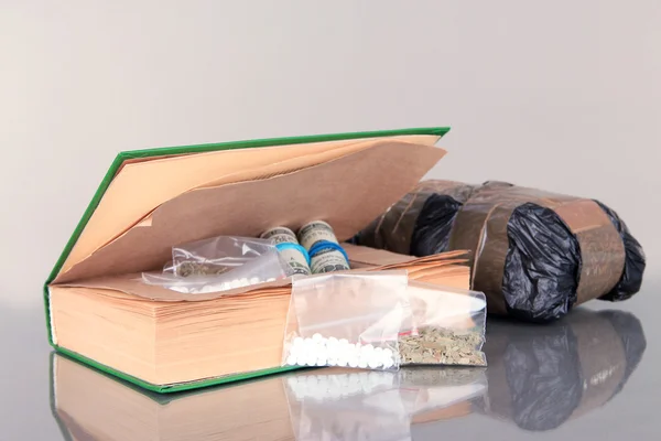 Narcotics in book-hiding place and packages on gray background — Stock Photo, Image