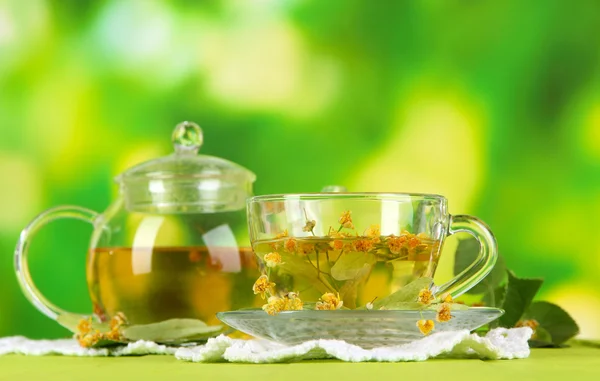 Kettle and cup of tea with linden on wooden table on nature background — Stock Photo, Image