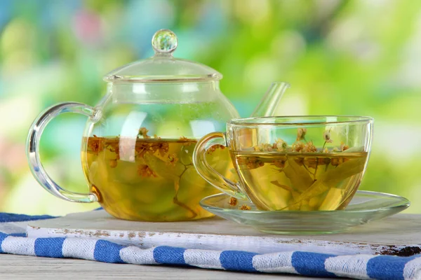 Kettle and cup of tea with linden on wooden table on nature background — Stock Photo, Image