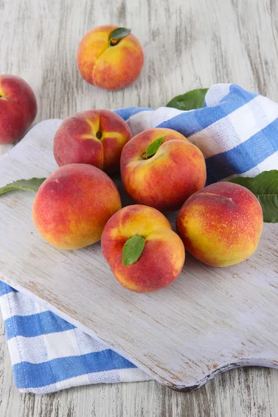 Peaches on board on napkin on table on wooden background — Stock Photo, Image