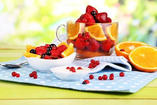 Nuttige fruitsalade in glas cup en kom op houten tafel op natuurlijke achtergrond — Stockfoto
