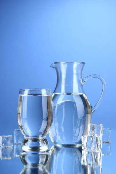 Jarra de vidrio de agua y vidrio sobre fondo azul — Foto de Stock