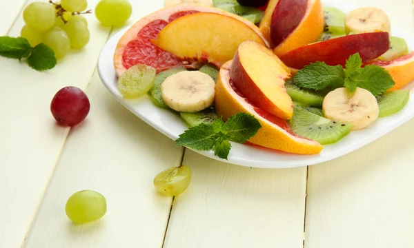 Surtido de frutas en rodajas en plato, sobre mesa de madera blanca — Foto de Stock