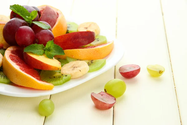 Surtido de frutas en rodajas en plato, sobre mesa de madera blanca — Foto de Stock
