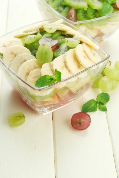 Tasty fruit salad in glass bowls, on white wooden table — Stock Photo, Image