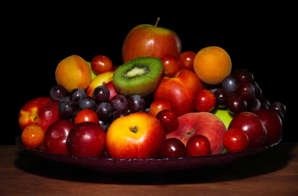 Assortment of juicy fruits on wooden table, on dark background — Stock Photo, Image