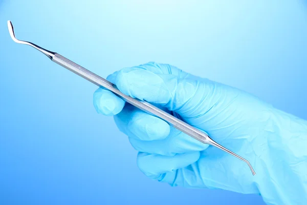 Hand in blauem Handschuh hält zahnärztliches Werkzeug auf blauem Hintergrund — Stockfoto