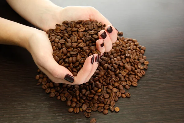 Mani femminili con chicchi di caffè, su sfondo di legno — Foto Stock