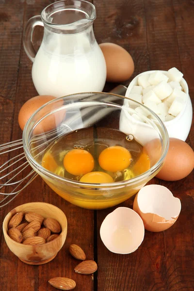 Broken egg in bowl and various ingredients next to them on wooden table close-up — Stock Photo, Image