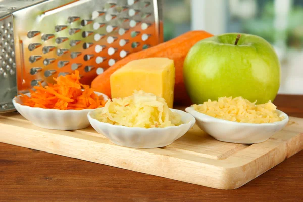 Grattugia in metallo e mela, formaggio, carota, sul tagliere, su sfondo brillante — Foto Stock