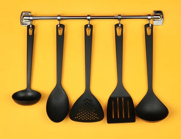 Černá kuchyně nádobí na stříbrné háčky, na žlutém podkladu — Stock fotografie